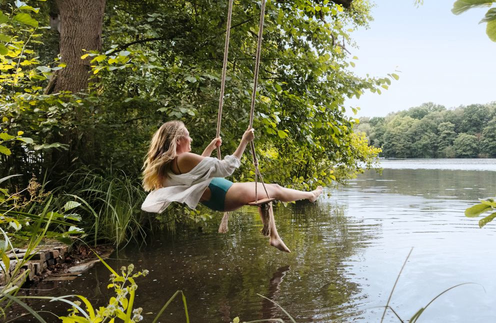 Frau schaukelt über einem See umgeben von grüner Natur