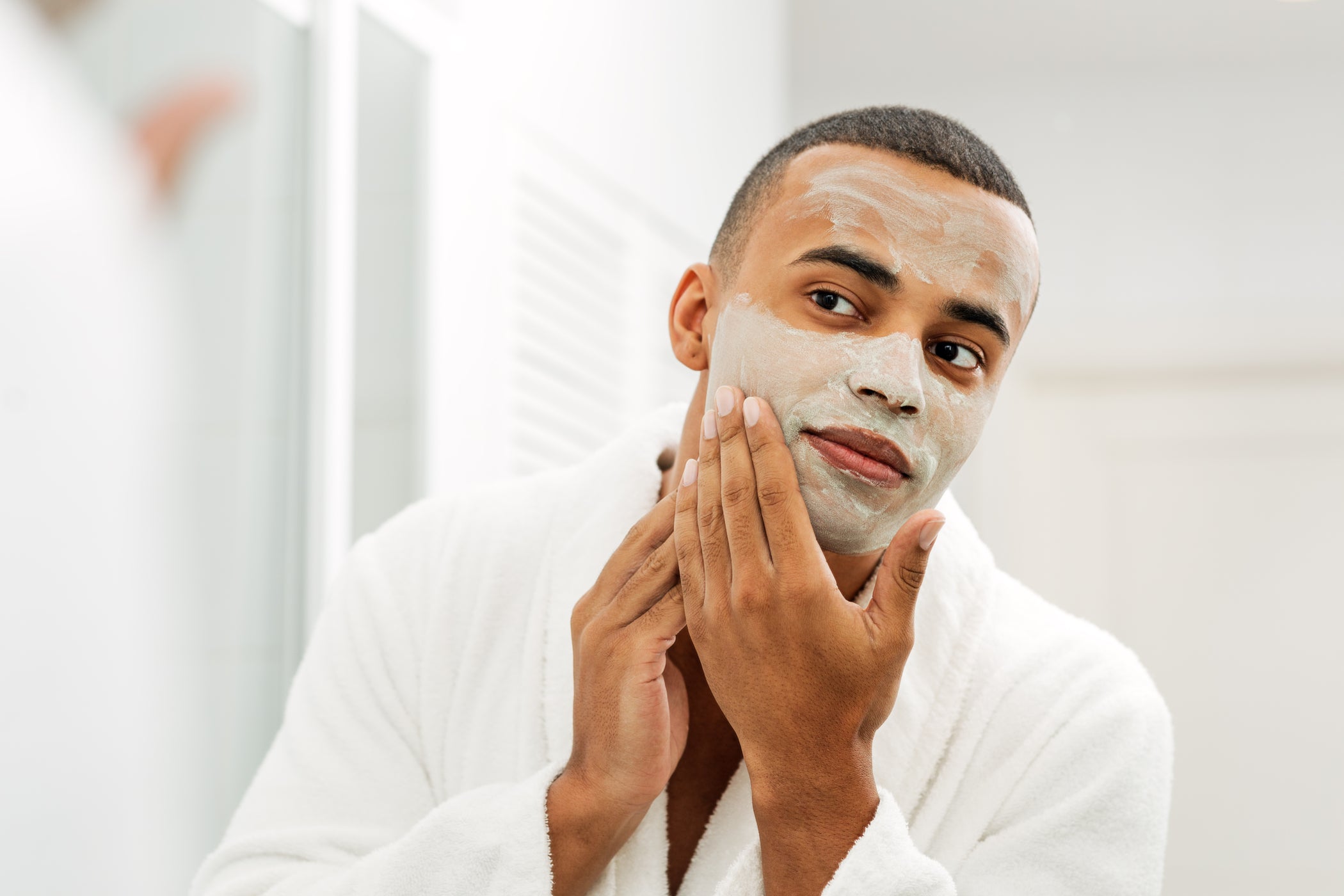 Jeune homme à la peau foncée applique un masque facial dans la salle de bain