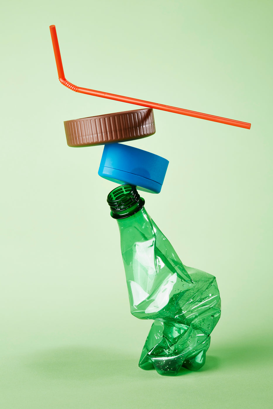 Bouteille plastique vide, bouchon et paille empilés sur fond vert