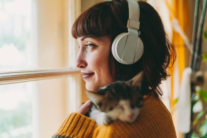 Femme avec écouteurs tient chat près de la fenêtre, lumière du jour chaude