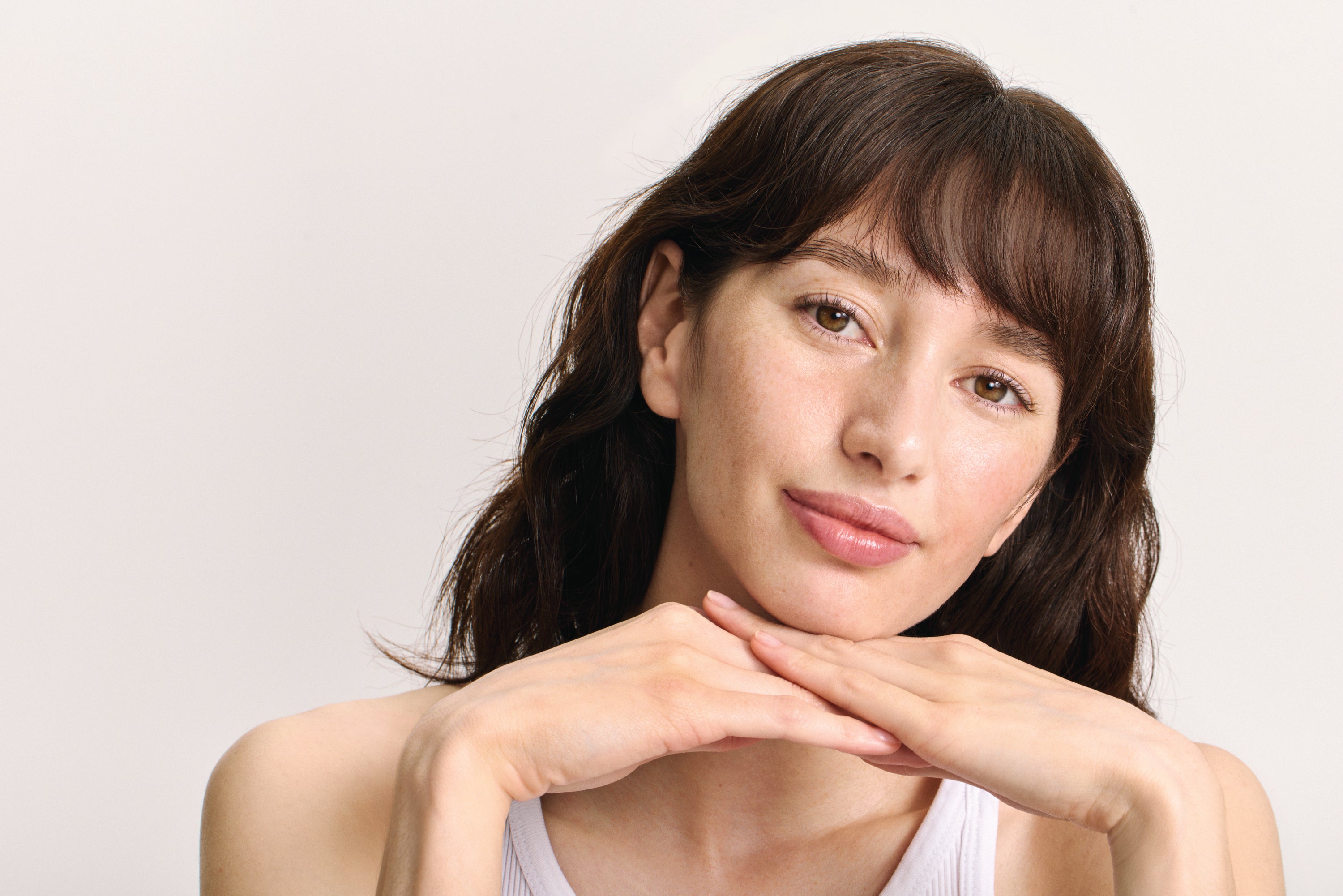 Femme aux cheveux foncés appuie sa tête sur ses mains et sourit à la caméra