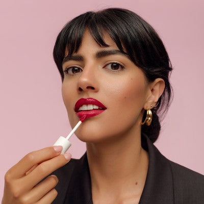 Femme appliquant un rouge à lèvres liquide rouge sur fond rose