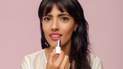 Femme appliquant un rouge à lèvres rose sur fond rose