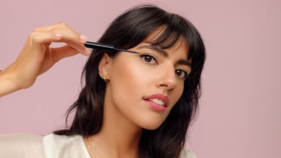 Femme applique eye-liner devant fond rose