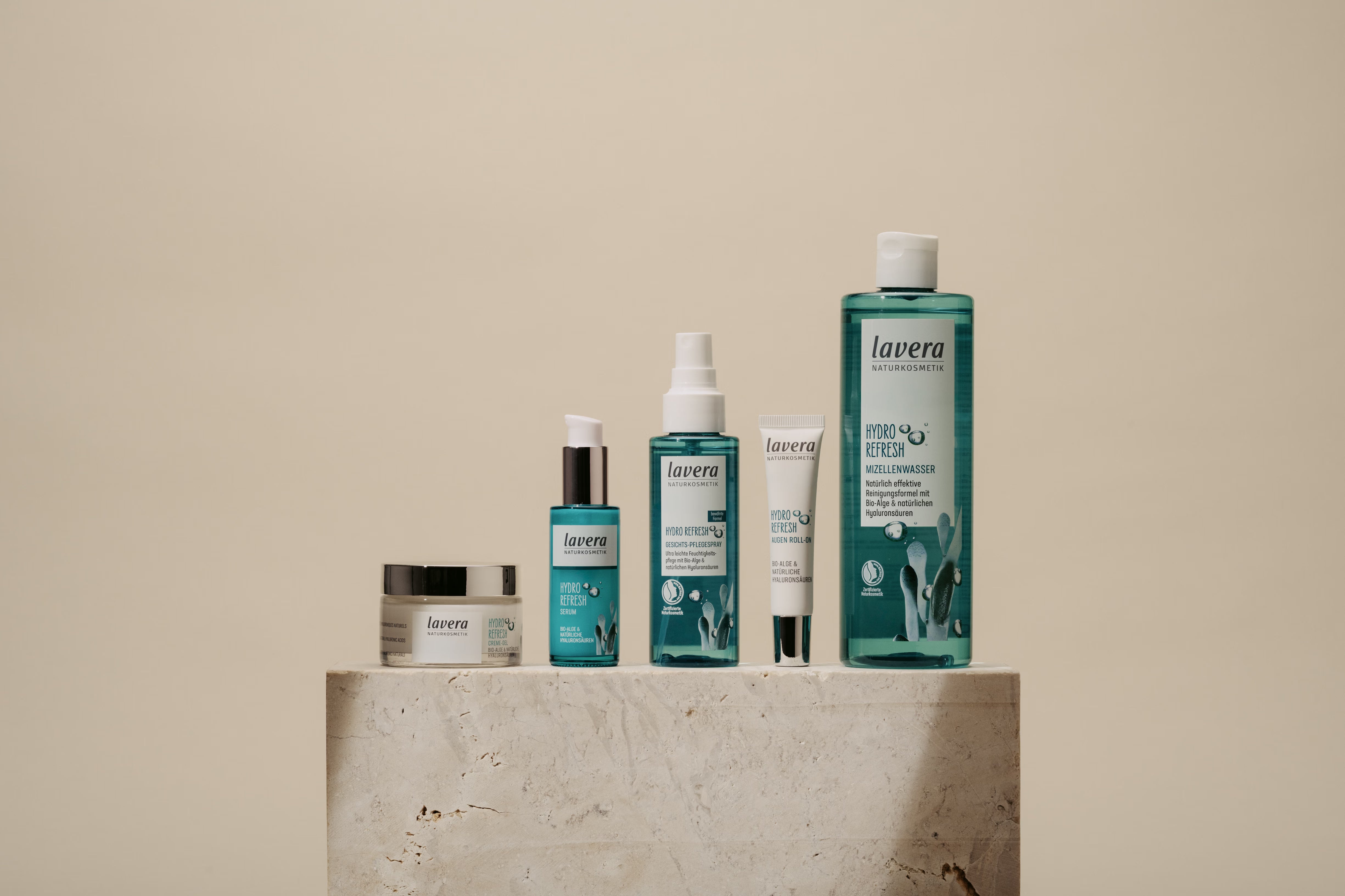 Sechs lavera Hydro-Refresh-Gesichtspflegeprodukte stehen auf einem steinernen Podest vor beigem Hintergrund.