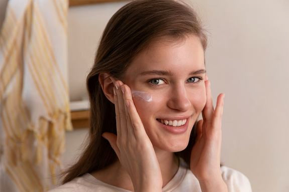 Femme applique fluide anti-UV sur la joue en souriant