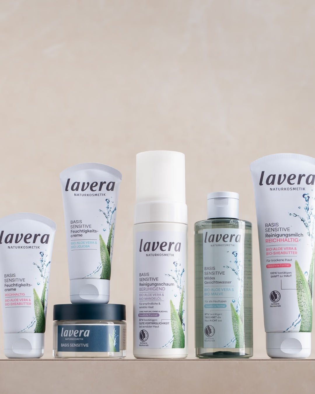 Sechs lavera Basis Sensitive Reinigungs- und Pflegeprodukte stehen vor einem hellen, beigefarbenen Hintergrund.