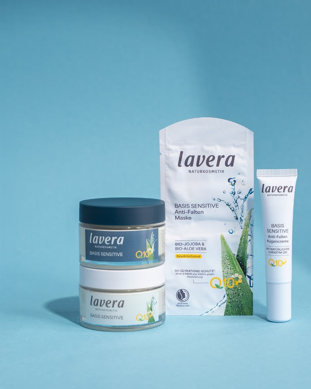 Vier lavera Basis Sensitive Anti-Falten-Produkte mit Q10 stehen vor hellblauem Hintergrund: zwei Cremetiegel, eine Tuchmaske und eine Augencreme.