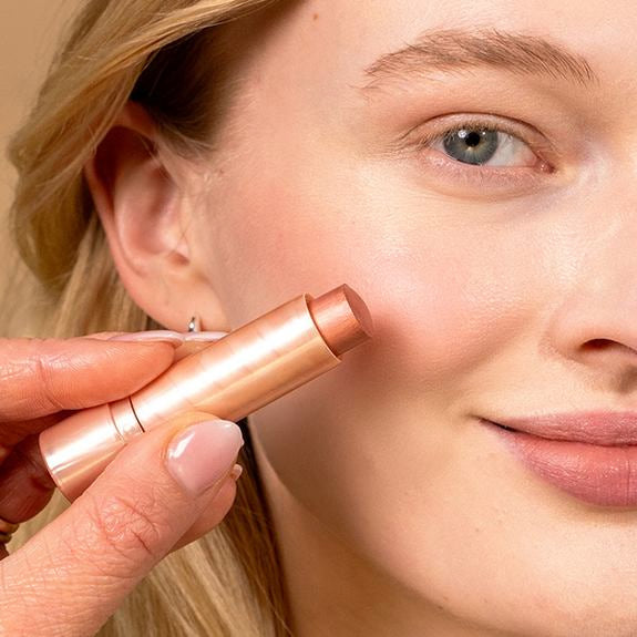 Gros plan d'une femme appliquant un stick blush sur la joue