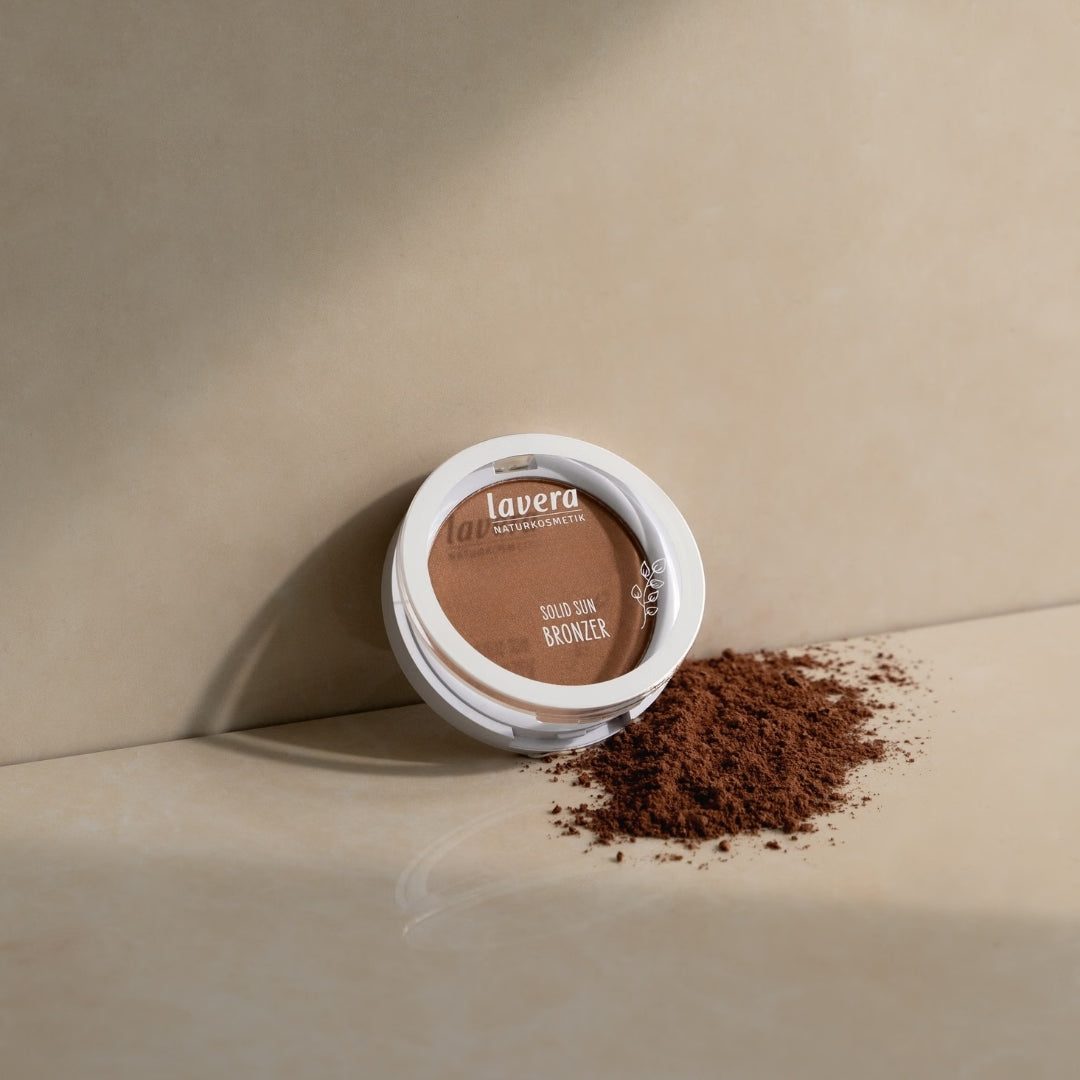 lavera Solid Sun Bronzer liegt auf einer beigefarbenen Oberfläche neben verstreutem Bronzerpuder.