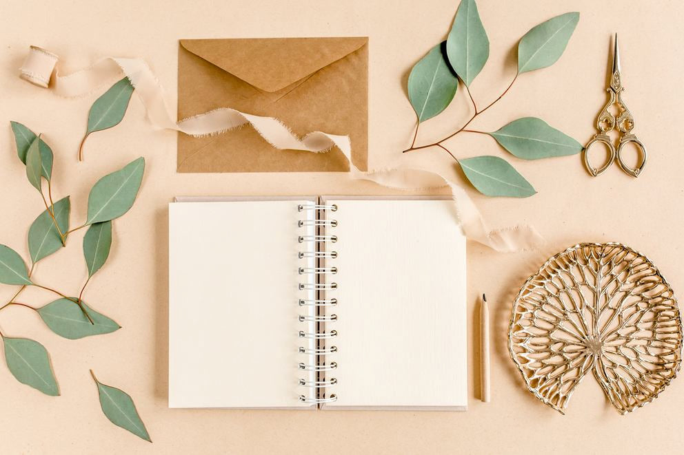 Carnet vierge avec enveloppe, feuilles d'eucalyptus, ciseaux et déco en flatlay