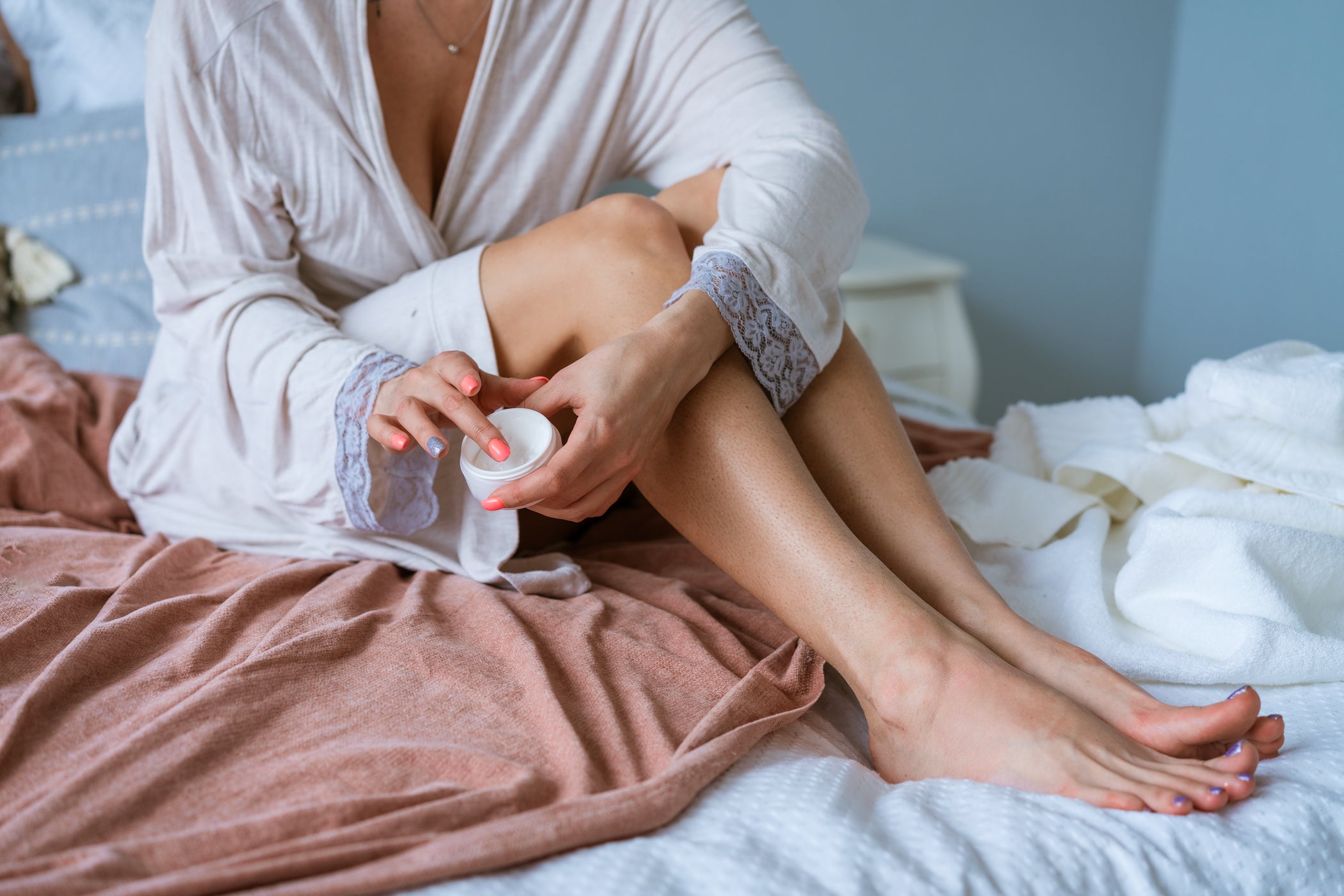 Femme en peignoir appliquant de la crème sur les jambes, assise sur le lit
