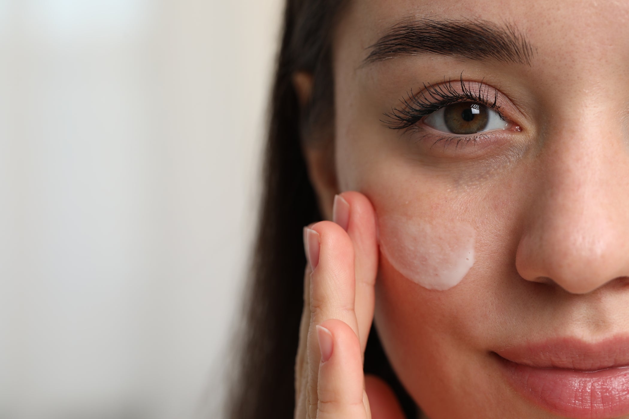 Gros plan : femme étale crème sur la joue, soin doux de la peau