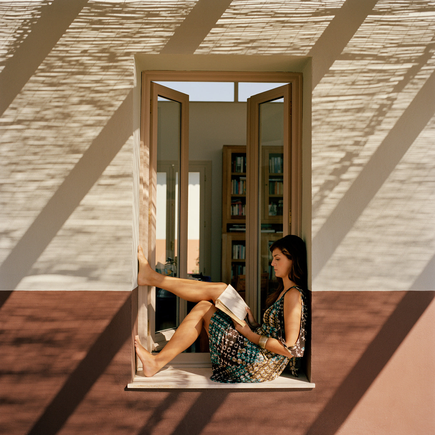 Femme aux longs cheveux bruns assise en train de lire près d'une fenêtre avec lumière naturelle et ombres