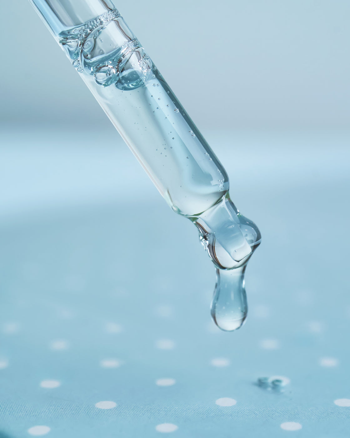 Pipette laisse tomber une goutte de sérum transparent, macro sur fond bleu