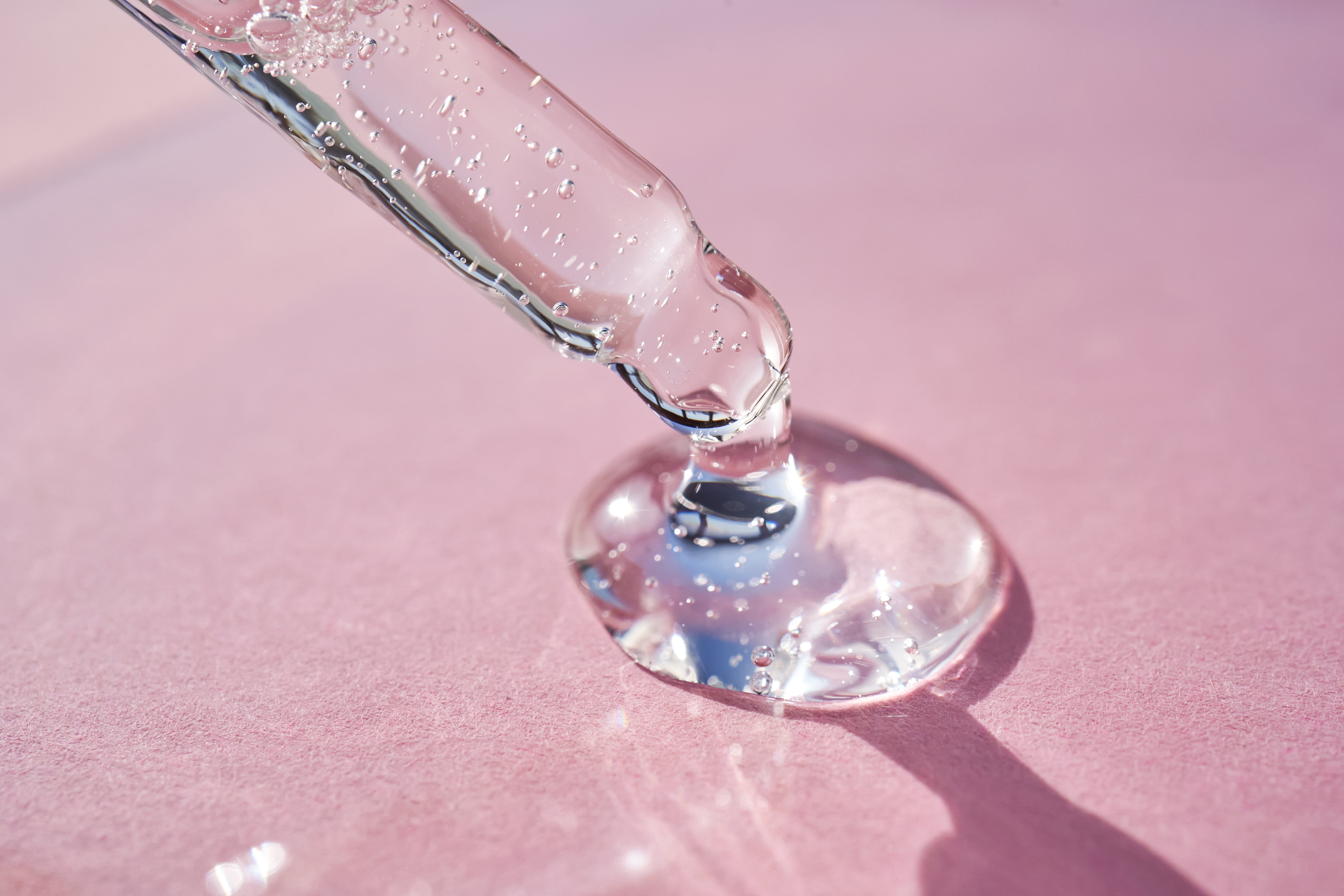 durchsichtiges Serum mit einer Pipette auf einen pinken Hintergrund getropft