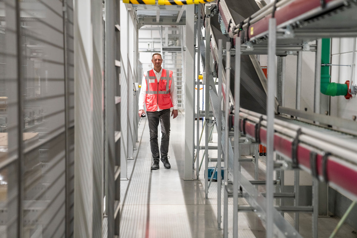 Homme en gilet rouge marchant dans un couloir du centre logistique lavera