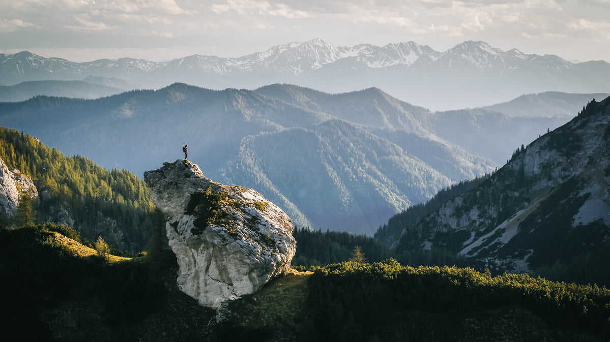 Personne debout sur un grand rocher dans un paysage montagneux verdoyant
