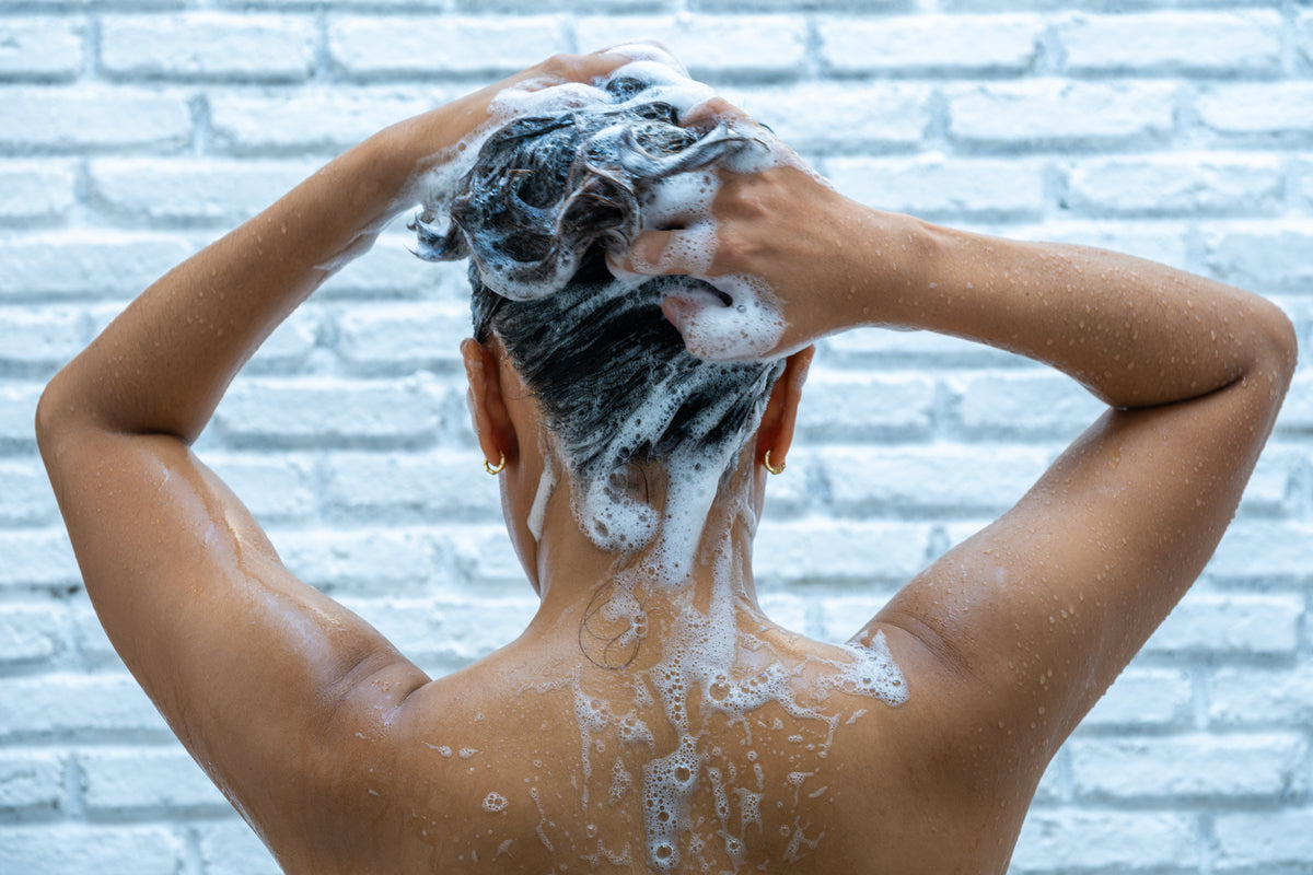 Personne de dos se lavant les cheveux avec beaucoup de shampooing moussant