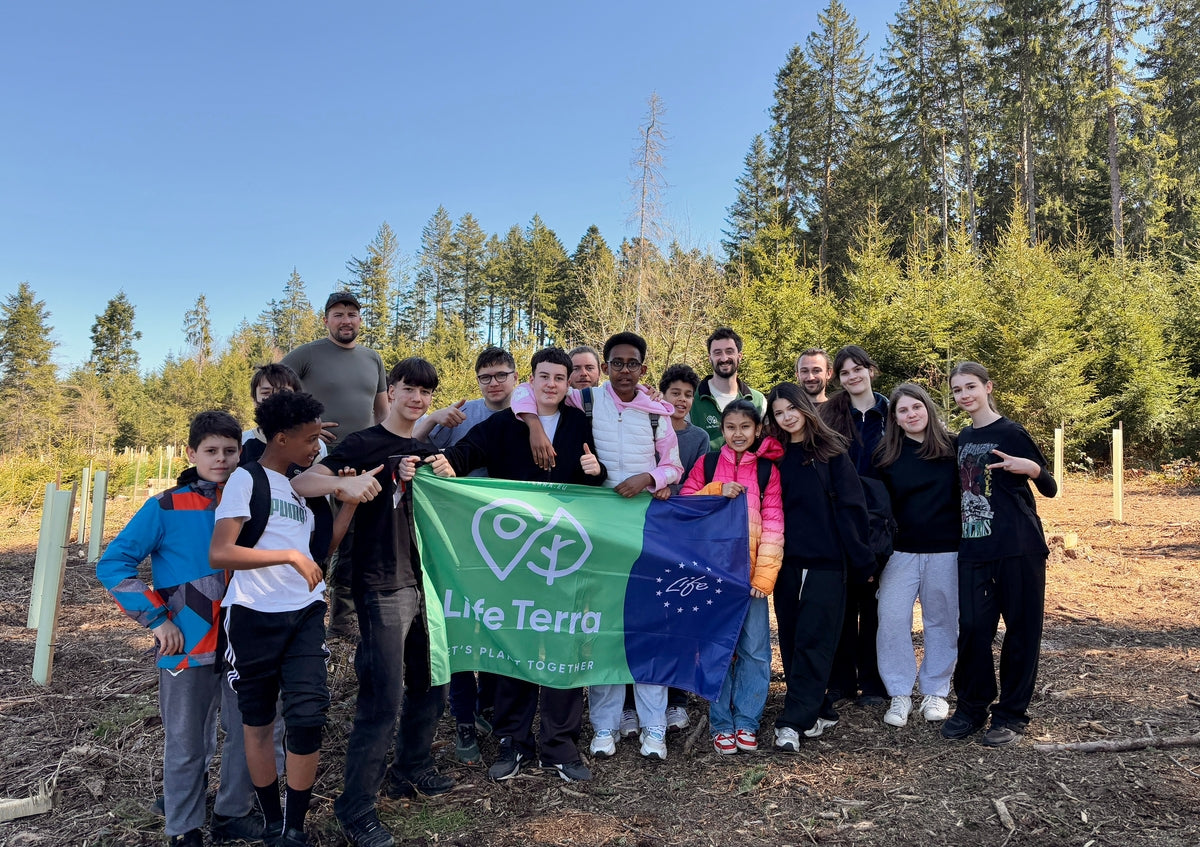 Groupe d'adultes et d'enfants dans la forêt avec un drapeau LifeTerra au centre