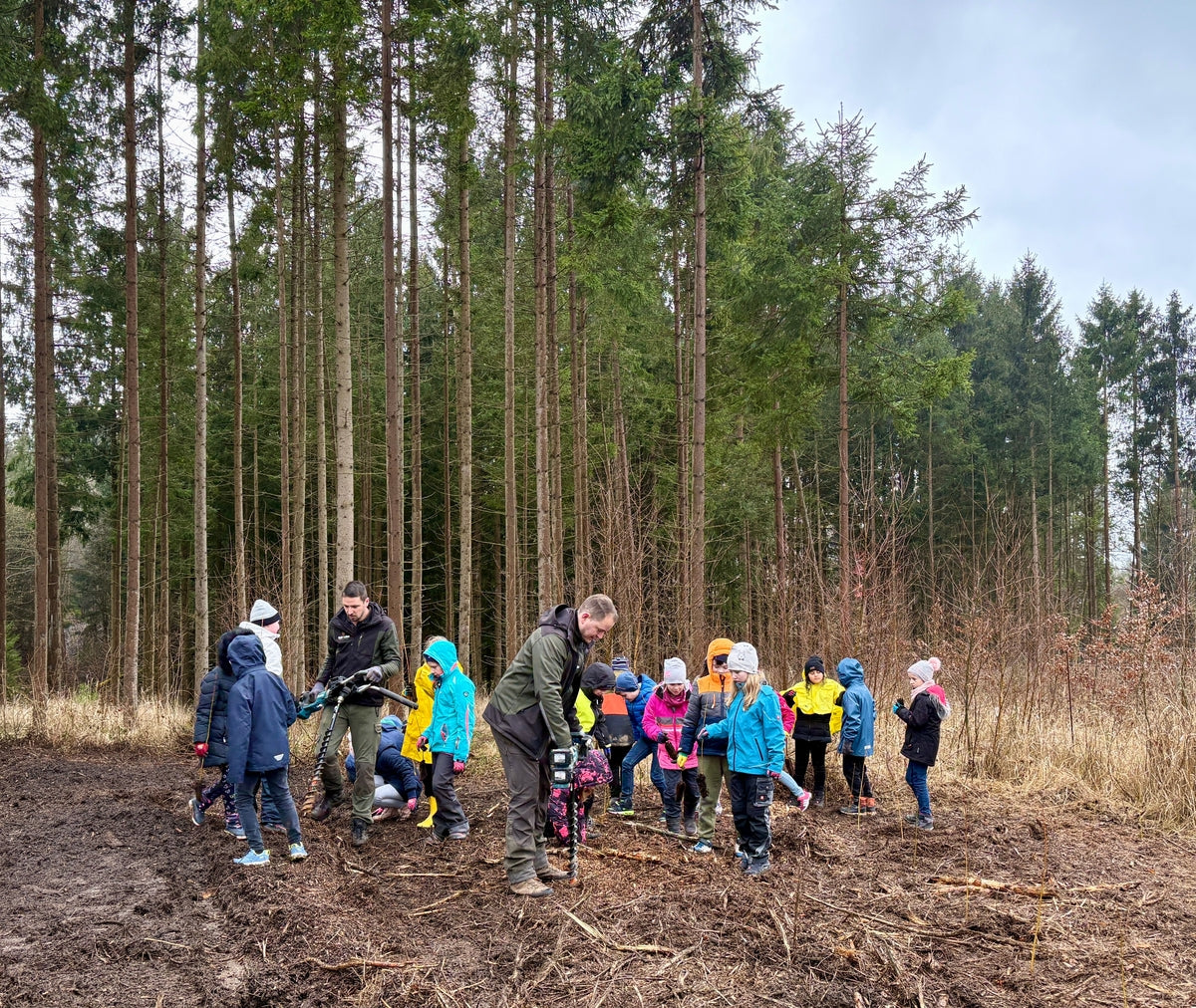 Groupe d'adultes et d'enfants en vestes colorées debout dans la forêt plantant des arbres