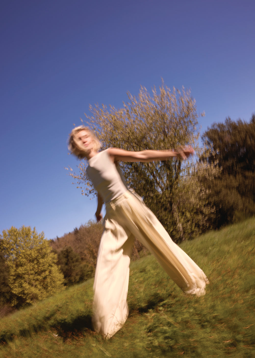 Femme en robe beige tourne sur elle-même bras écartés dans la nature – expression de joie de vivre et d'équilibre intérieur