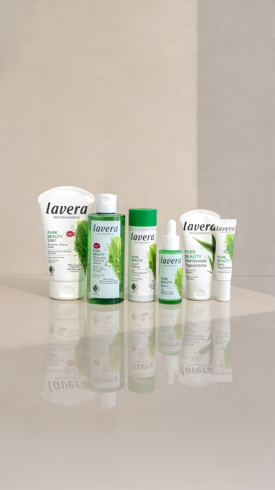 lavera Pure Beauty Gesichtspflegeprodukte stehen auf einer spiegelnden Oberfläche vor einem hellen, zweigeteilten Hintergrund.