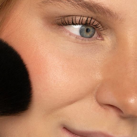 Application de blush en poudre sur la joue avec pinceau