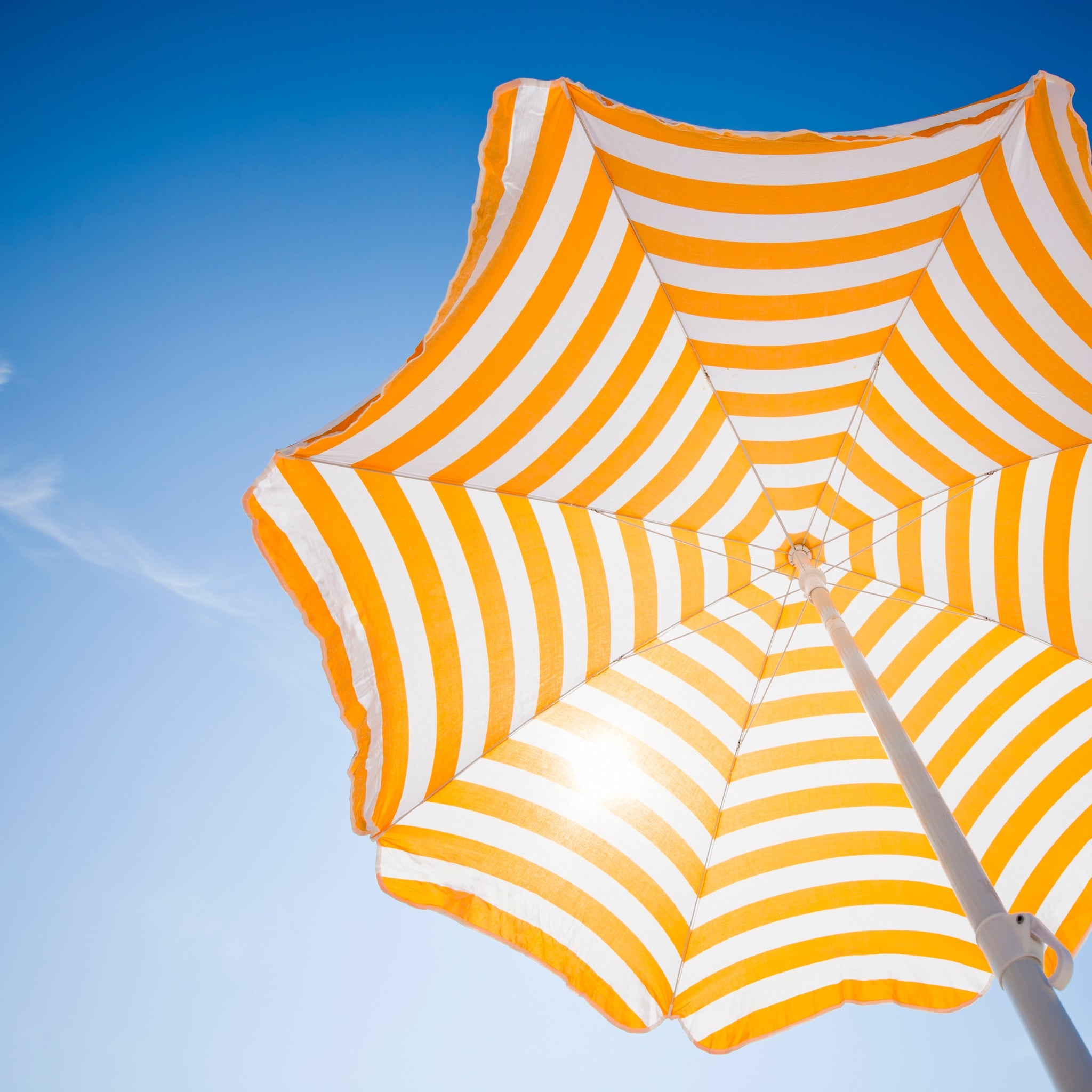 Parasol rayé jaune et blanc photographié d'en bas devant un ciel bleu.