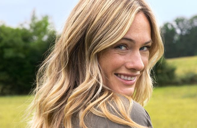 Femme blonde souriante regardant par-dessus l'épaule dans la verdure