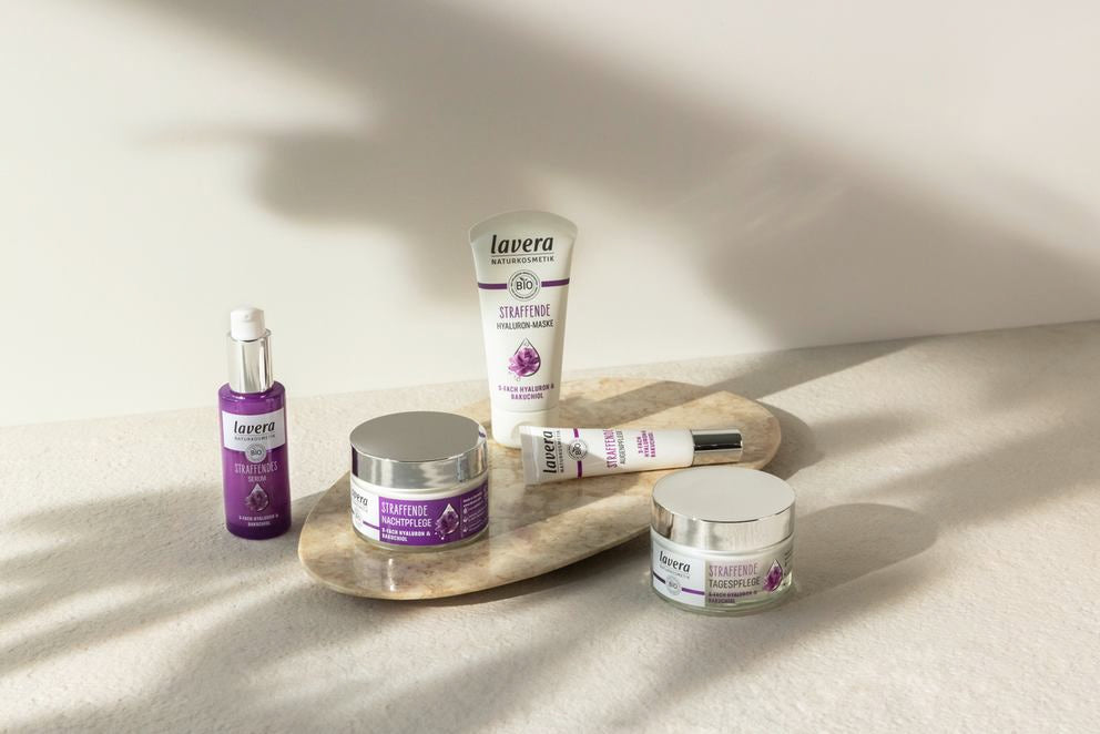 Gamme de soins raffermissants avec cinq produits violets lavera sur pierre