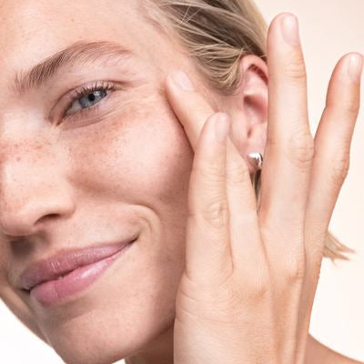 Une femme blonde passe un doigt sur sa joue et sourit