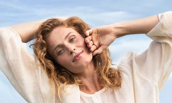 Femme aux cheveux bouclés profite du soleil les yeux fermés