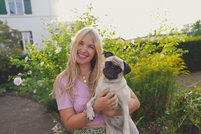 Femme blonde souriante tenant un carlin dans ses bras