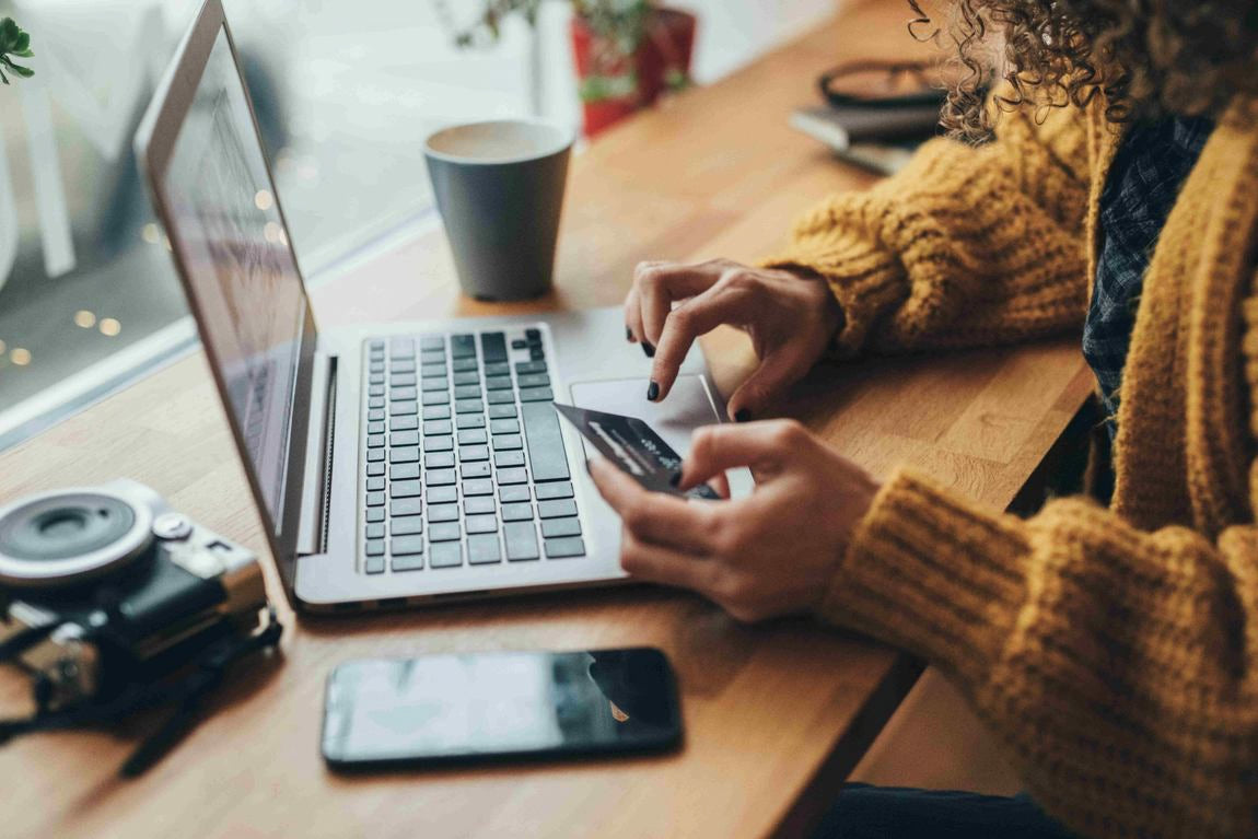 Frau hält Kreditkarte am Laptop, Online-Zahlung am Schreibtisch