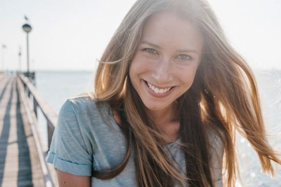 Femme souriante aux cheveux longs sur une jetée au bord de la mer