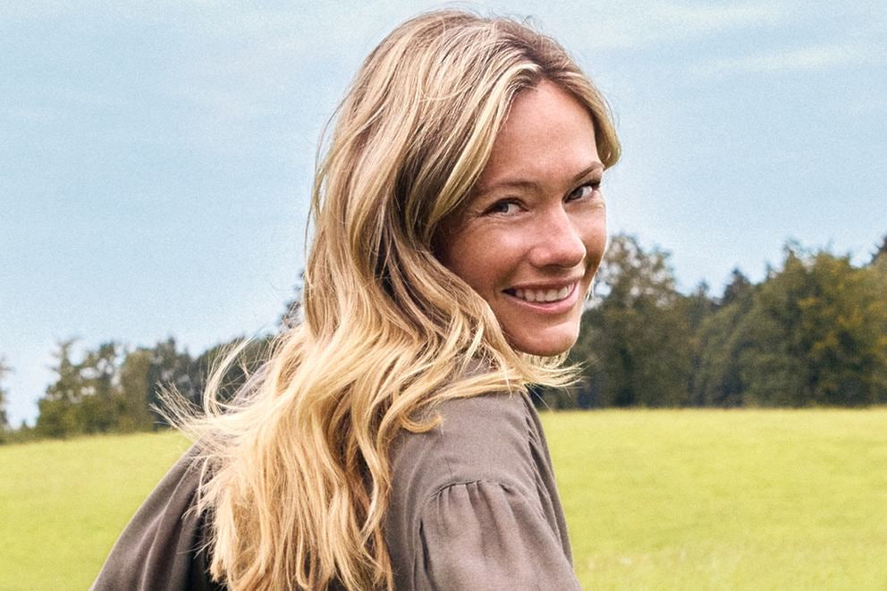 Lächelnde blonde Frau blickt über die Schulter auf einer grünen Wiese