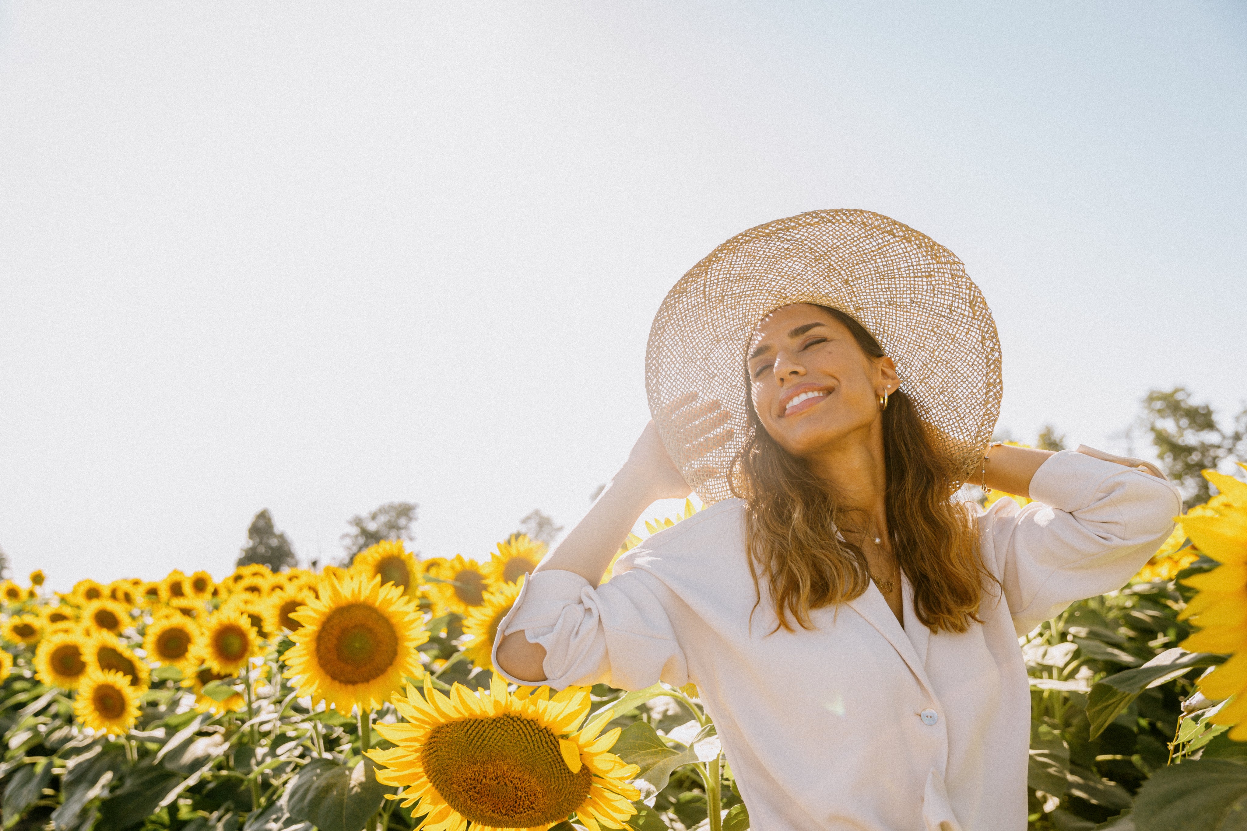 Femme avec chapeau de paille dans champ de tournesols, regarde vers le soleil, ambiance estivale
